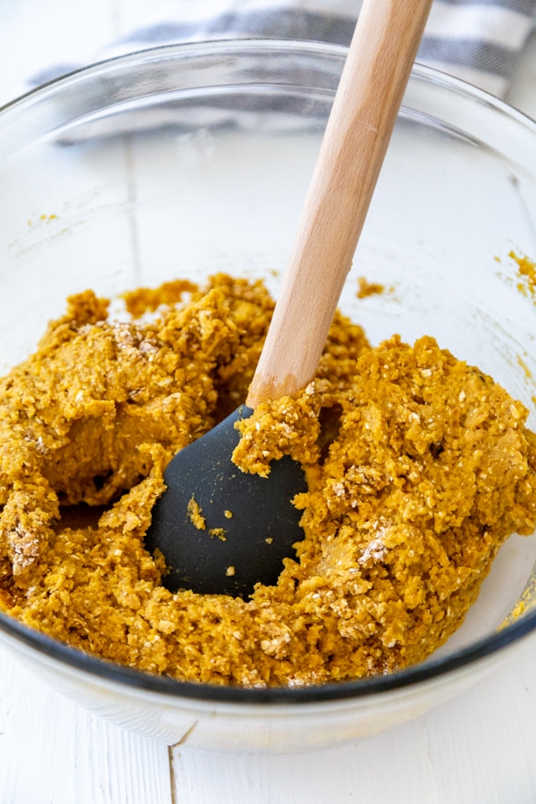 Pumpkin blondie batter being stirred with a spatula in glass bowl.