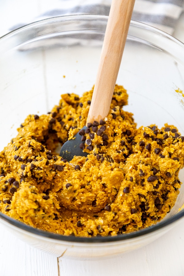 A glass bowl with a wood spatula stirring chocolate chips into pumpkin blondie batter.