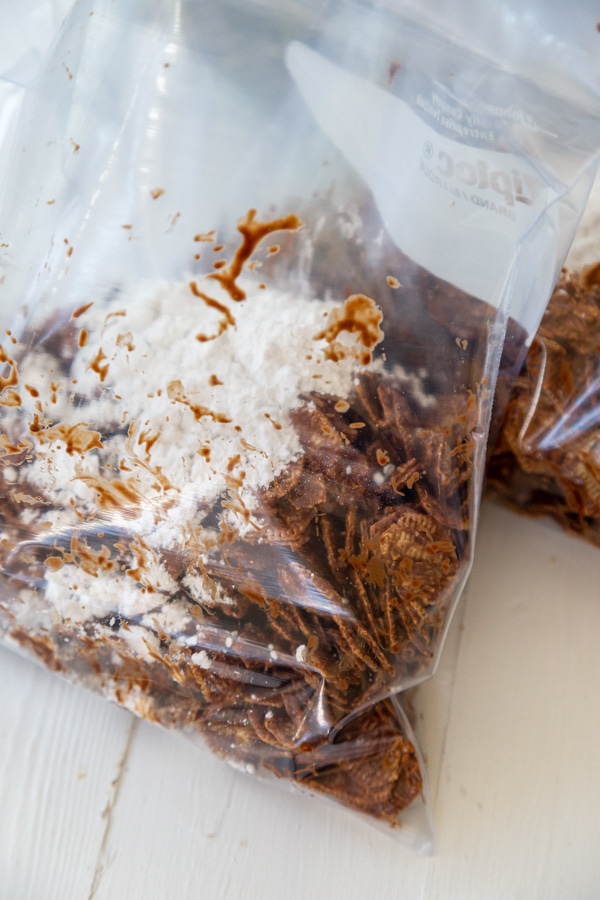A plastic bag with chocolate covered cereal and powdered sugar.