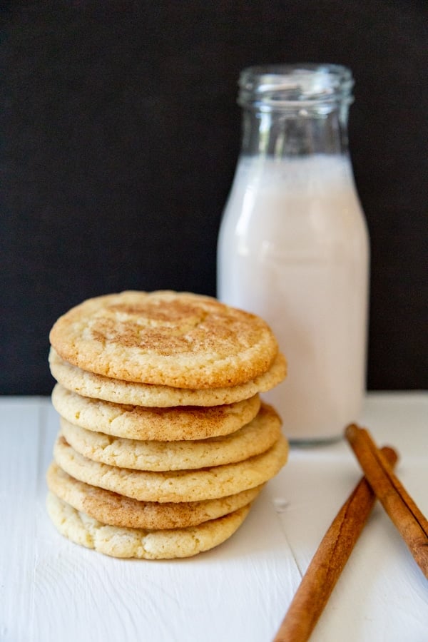 A stack of cookies and a bottle of milk with cinnamon sticks next to it.