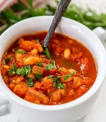 A bowl of tomato and white bean soup with a silver spoon in the bowl.