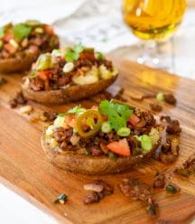 Three loaded stuffed potatoes on a wood board with a glass of beer.