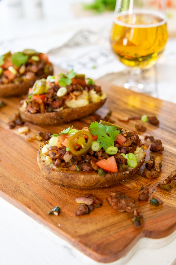 Three loaded stuffed potatoes on a wood board with a glass of beer.
