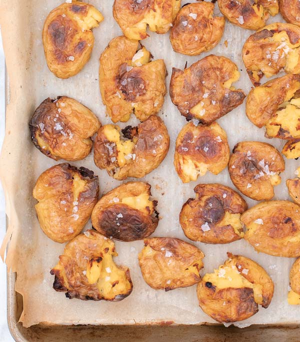 Smashed potatoes with salt on a parchment lined baking sheet. 