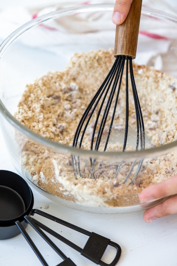A glass bowl with oats, flour, and spices being whisked together.