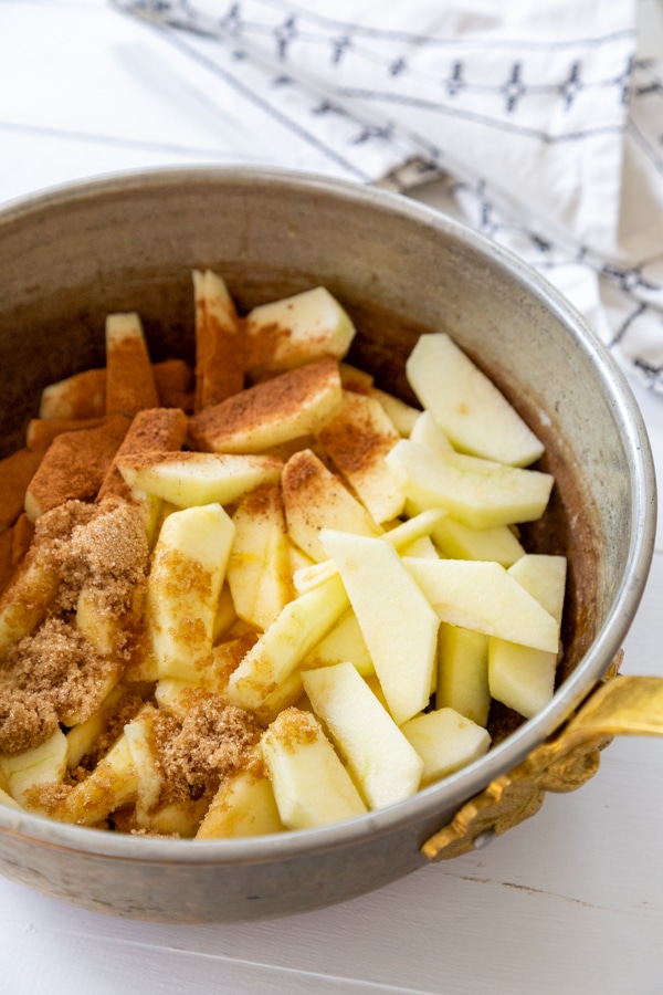 A copper pot with sliced apples and cinnamon.