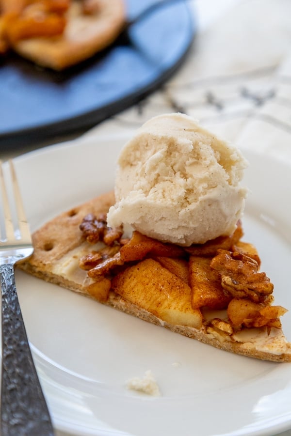 A slice of apple pie pizza with a scoop of vanilla ice cream on a white plate.