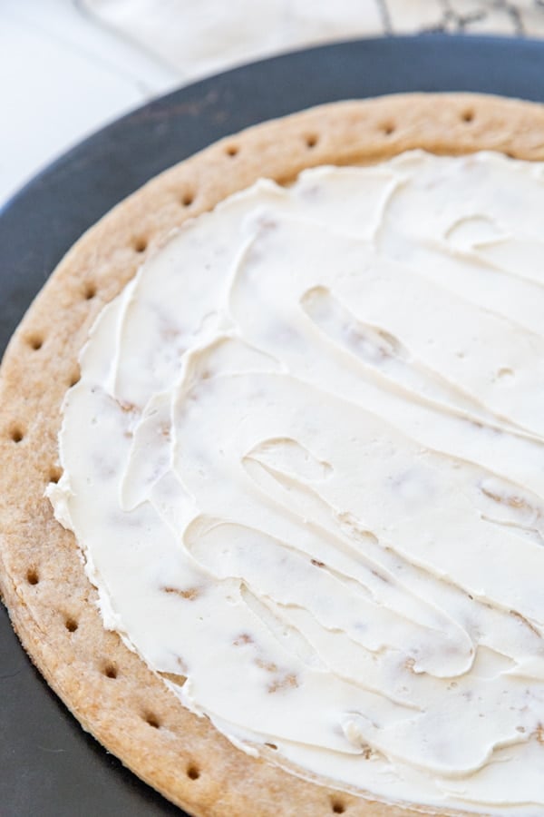 A pie crust on a pizza stone with cream cheese spread on the top.