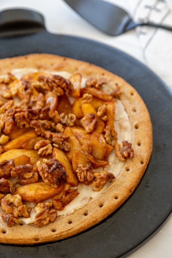 A baked apple pie pizza on a black pizza stone.