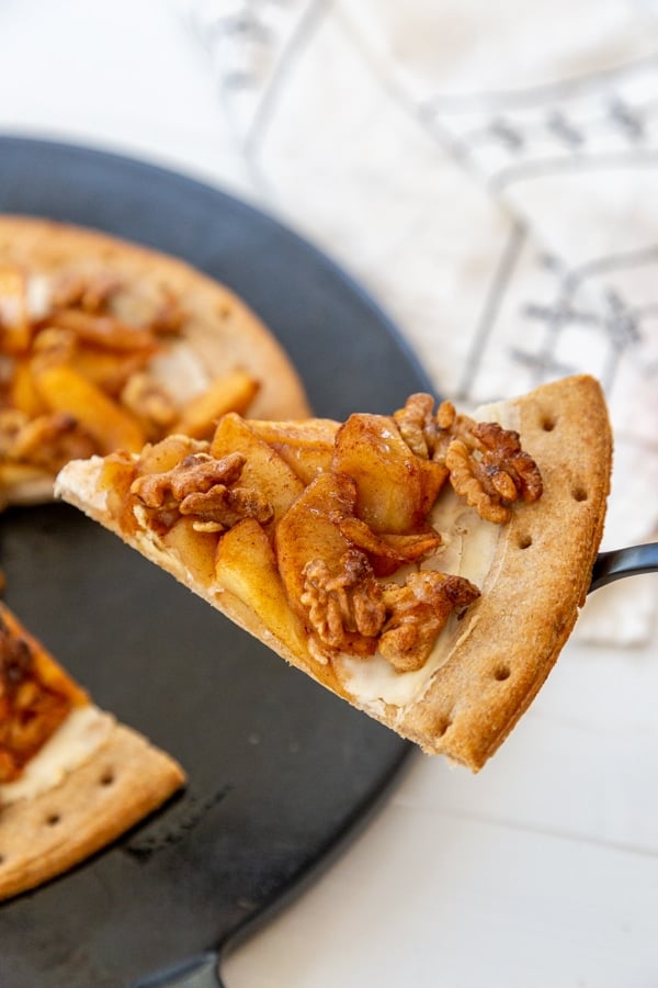 A slice of apple pizza on a serving utensil being lifted from the pizza stone. 