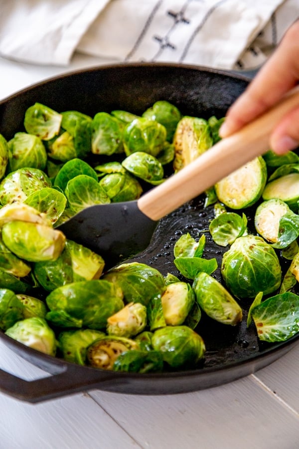 A hand stirring oil and Brussels sprouts in a skillet.