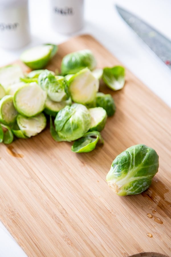 A whole and several halved Brussels sprouts on a wood cutting board.