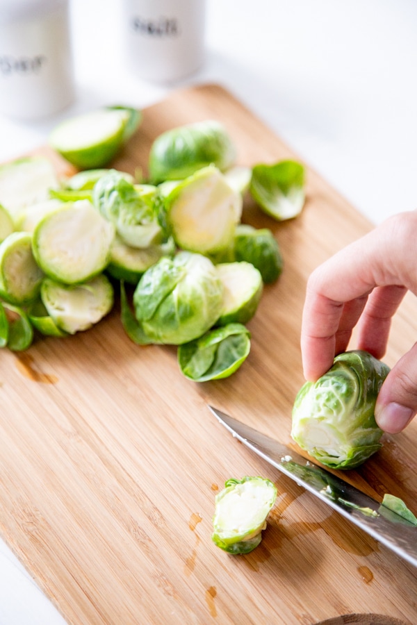 Two hands cutting the end off of a Brussels sprout.
