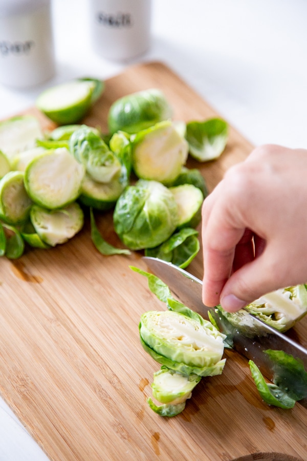 A person slicing a Brussels sprout in half with other halved sprouts on a wood board.