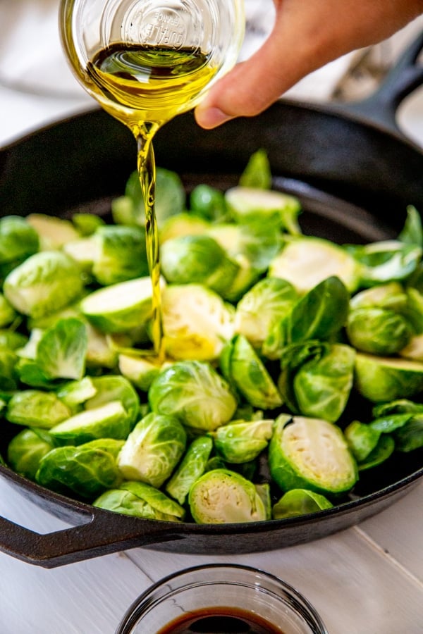 A hand drizzling olive oil over a skillet of Brussels sprouts.