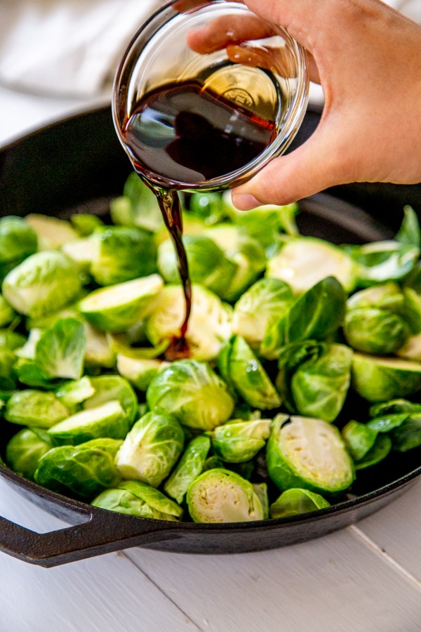 A hand pouring balsamic glaze over a pan of Brussels sprouts.