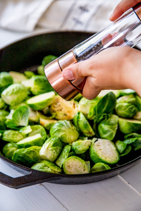 Hands grinding pepper over a pan of Brussels sprouts.