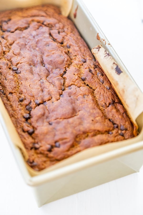 A loaf of chocolate chip pumpkin bread in a bread pan with parchment paper.