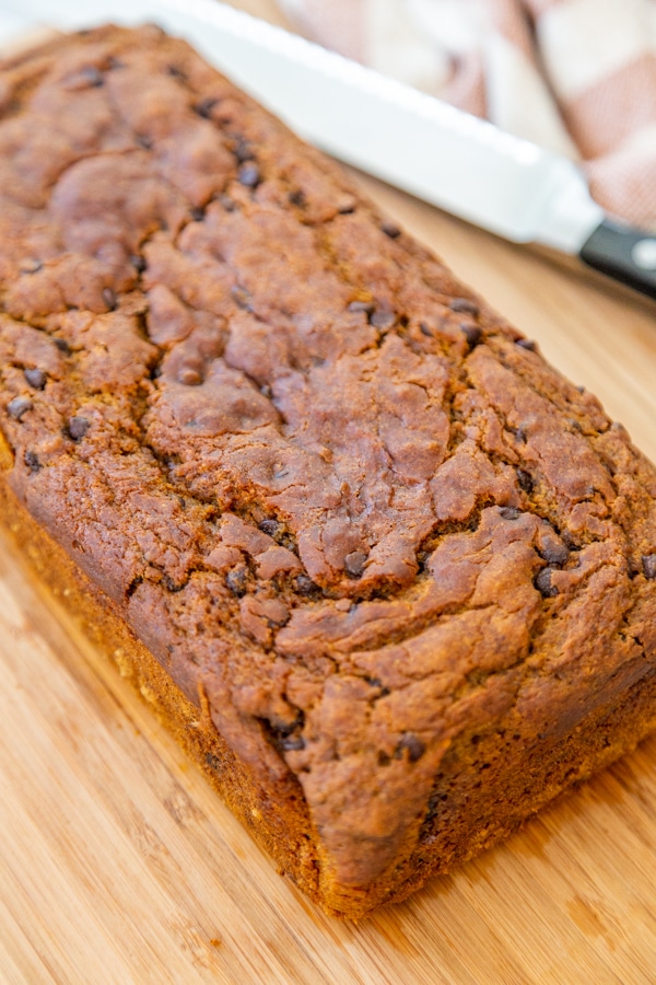 A loaf of pumpkin chocolate chip bread on a wood board. 