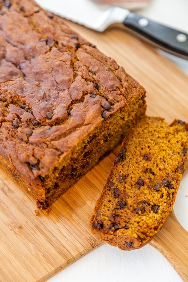 A slice of chocolate chip pumpkin bread and the loaf of bread on a wood board. 