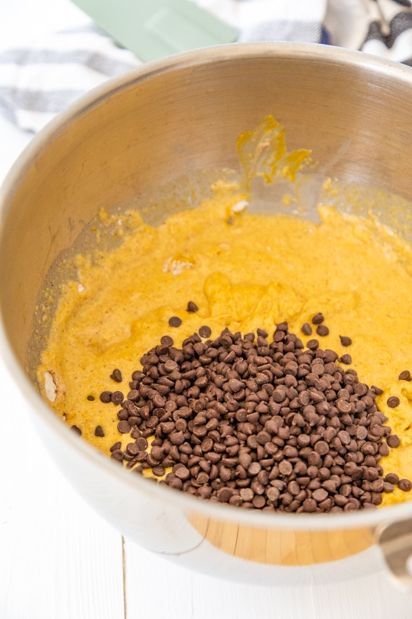 A silver mixing bowl with pumpkin bread batter and chocolate chips.