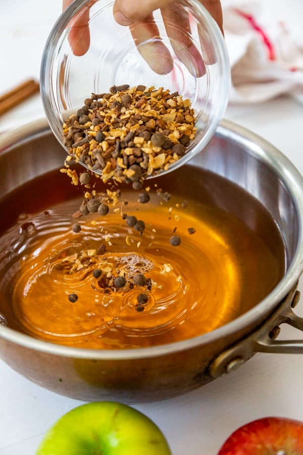 A hand pouring mulling spices into a pot of apple cider. 