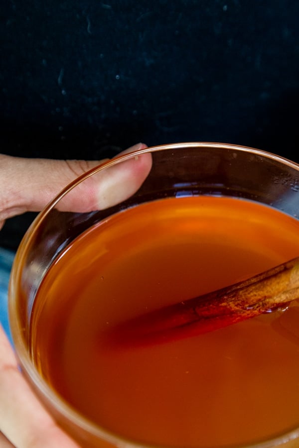 A hand holding a glass mug of cider. 