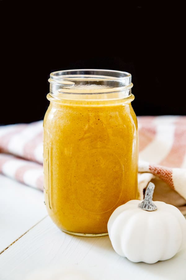 A pumpkin smoothie in a mason jar with a small white pumpkin next to the jar. 