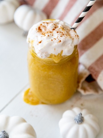 An overhead shot of a pumpkin smoothie with whipped cream and cinnamon and a black and white straw.