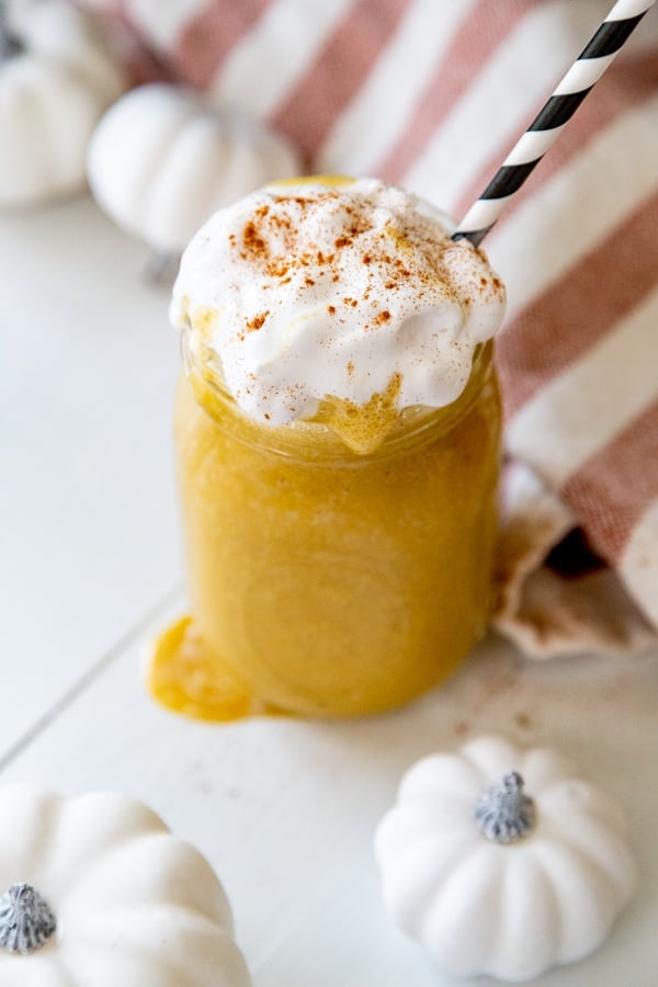 An overhead shot of a pumpkin smoothie with whipped cream and cinnamon and a black and white straw. 