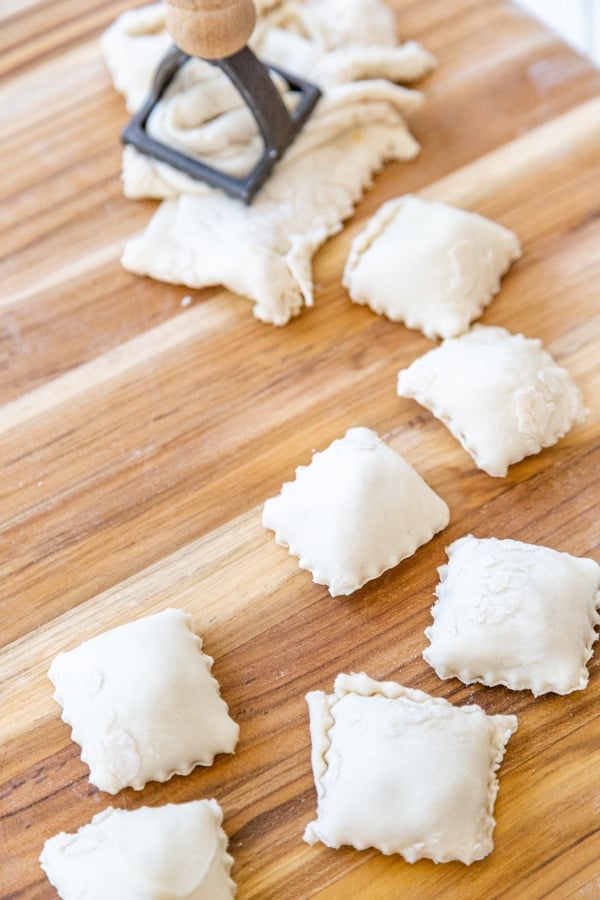 A wood board with homemade ravioli and a ravioli press. 