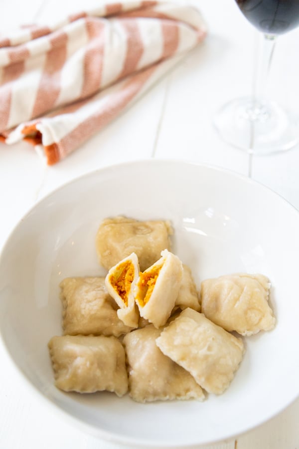 A bowl of pumpkin ravioli with one ravioli cut in half.