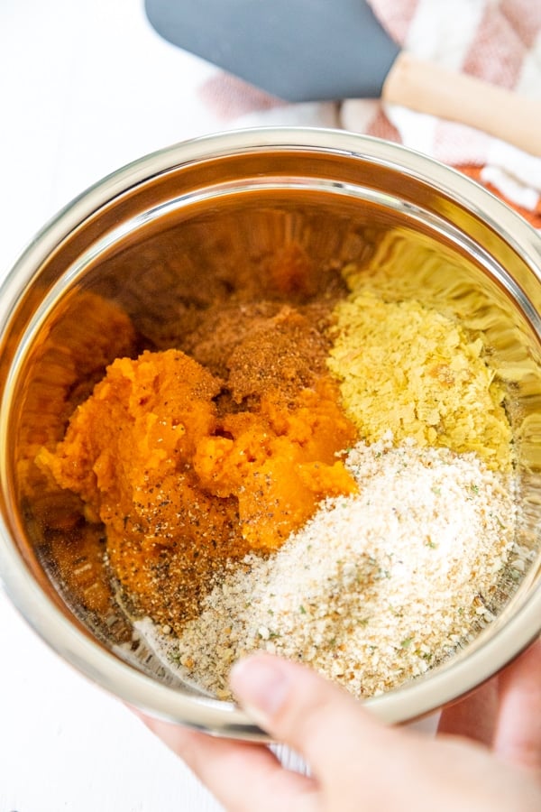 A hand holding a bowl of pumpkin puree, breadcrumbs, and spices.