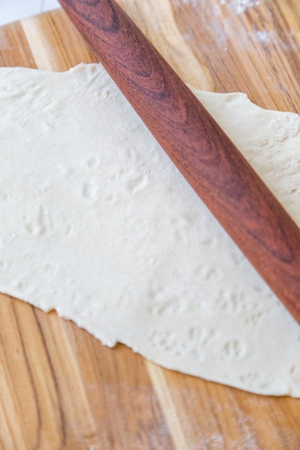 Pasta dough rolled out with a wood rolling pin on a wooden board.