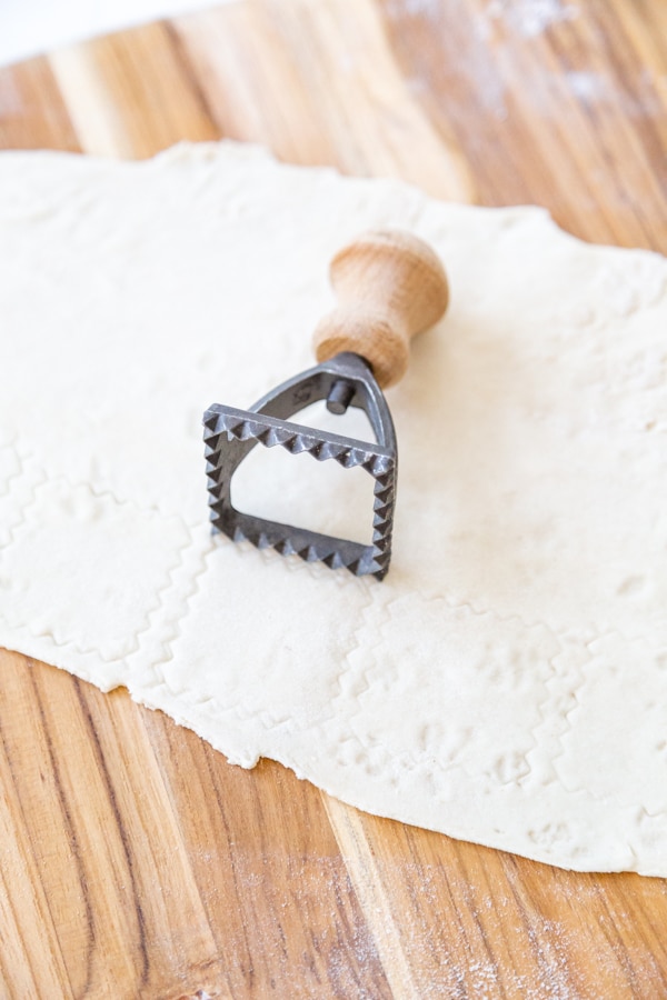 A ravioli press marking a rolled out piece of pasta dough.