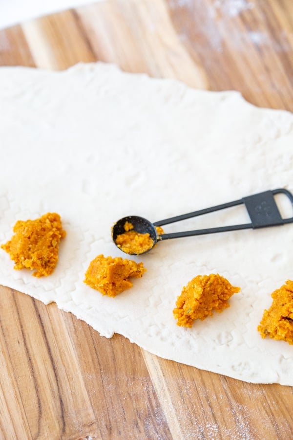 A black measuring spoon with dollops of pumpkin filling on a sheet of pasta dough.