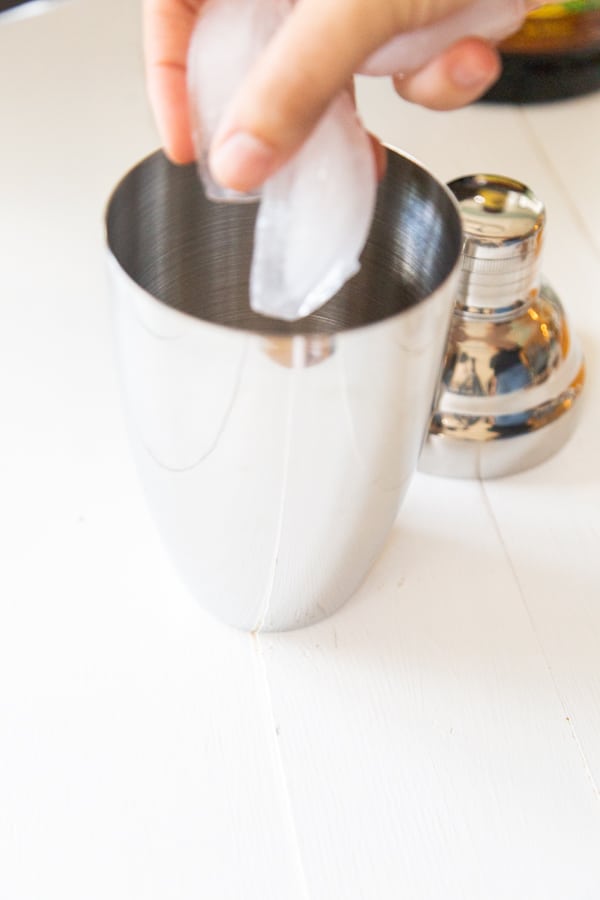 A hand putting ice cubes into a martini shaker.