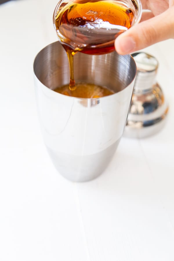 A hand pouring maple syrup into a martini shaker.