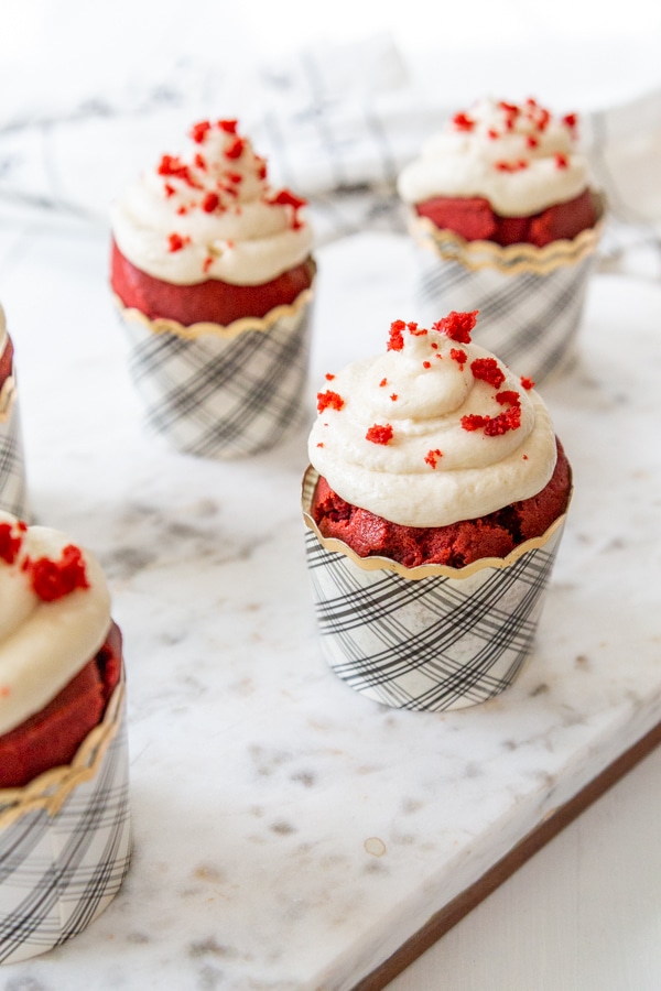 Red velvet cupcakes with cream cheese frosting on a marble board.