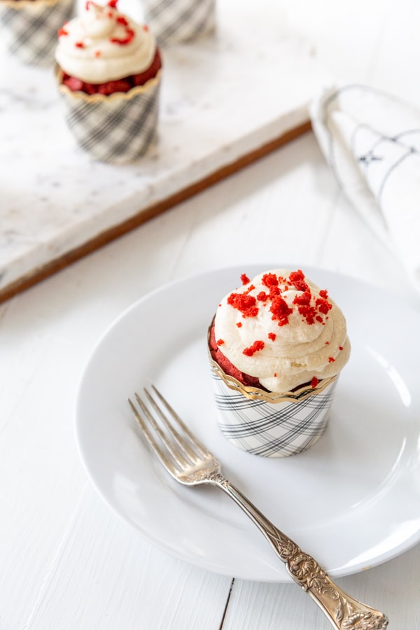 A red velvet cupcake with cream cheese frosting and red cake crumbs sprinkled on top. 