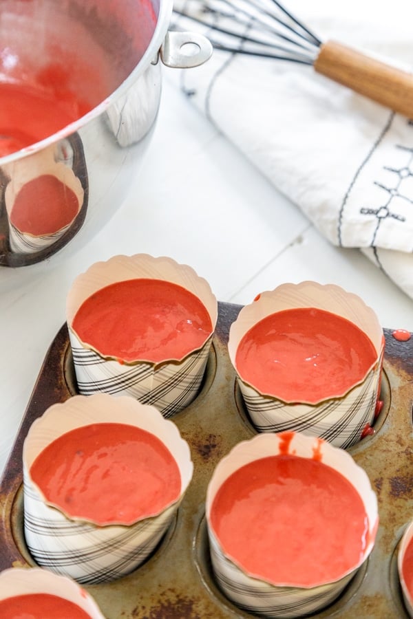 Cupcake liners in a muffin tin filled with red cake batter.