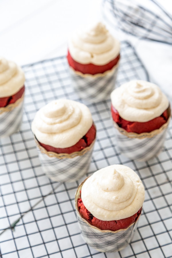 Red velvet cupcakes with piped cream cheese frosting on a wire cooling rack. 