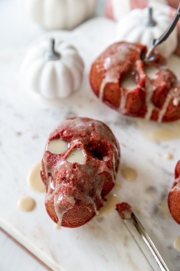 Mini skull cakes with icing dripping down the sides and a white pumpkin next to them.