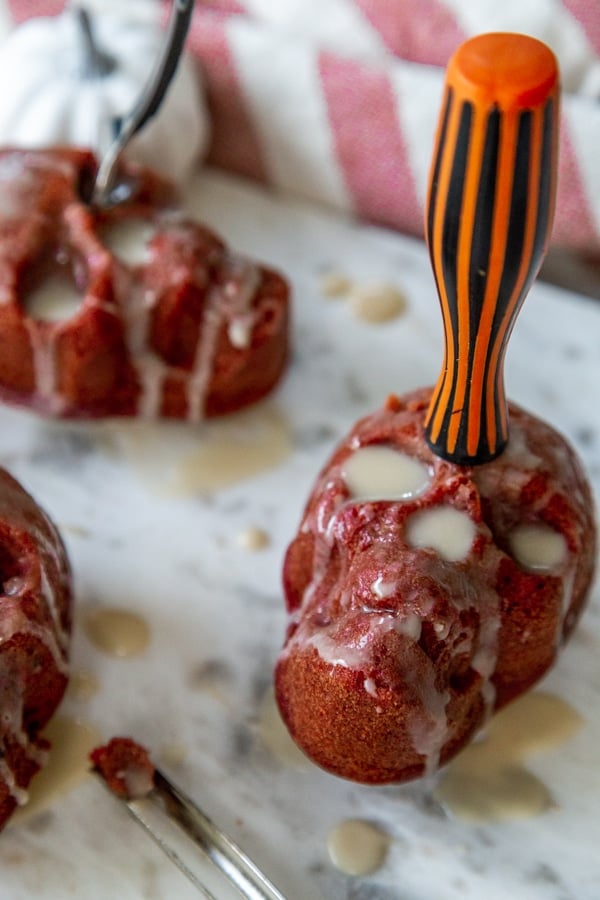 Skull cakes with icing dripping down the sides and a knife sticking out of the top of the cake.