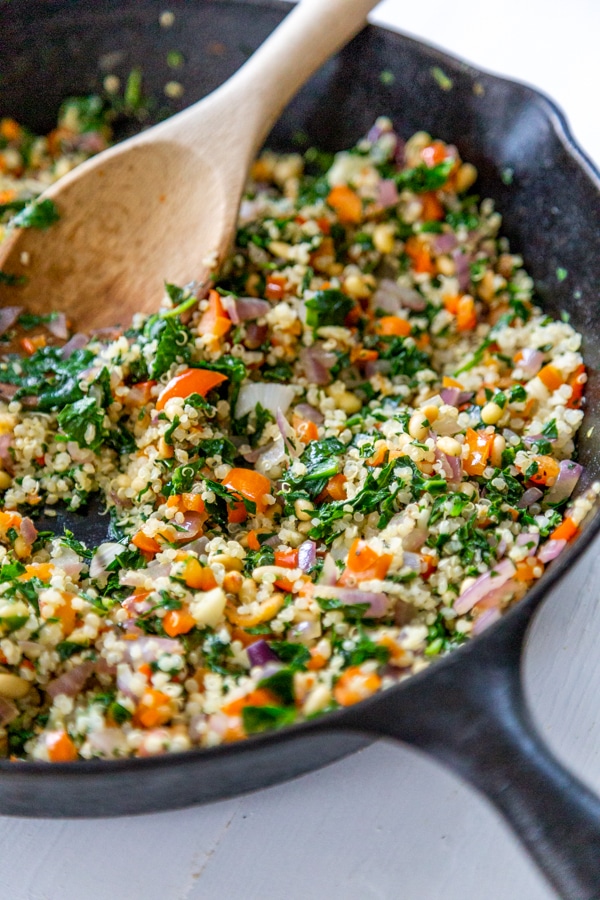 An iron skillet with quinoa and vegetables and a wooden spoon.