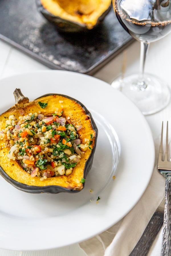 Stuffed acorn squash on a white plate with squash in the background.
