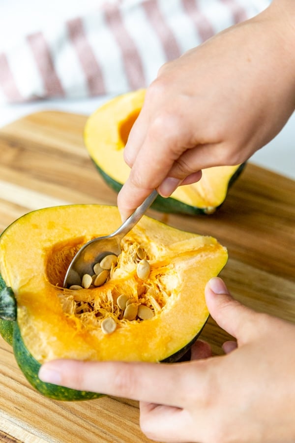A hand scooping the seeds out of an acorn squash with a spoon.