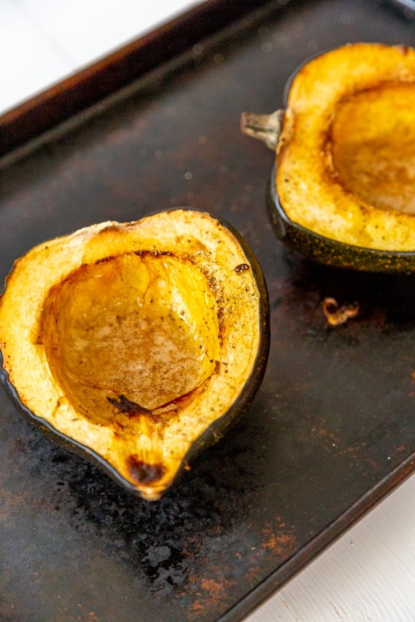 Two halves of roasted acorn squash on a baking sheet.