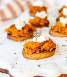 A marble and wood board with sweet potato canapes topped with ricotta.