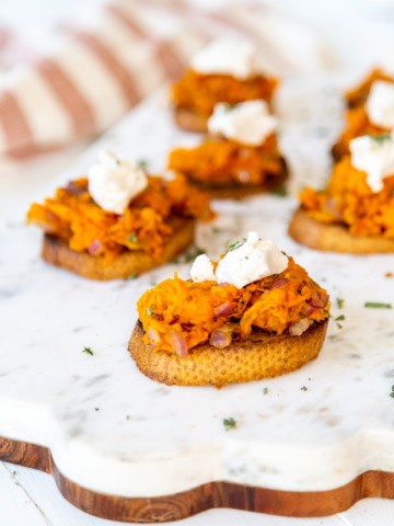 A marble and wood board with sweet potato canapes topped with ricotta.